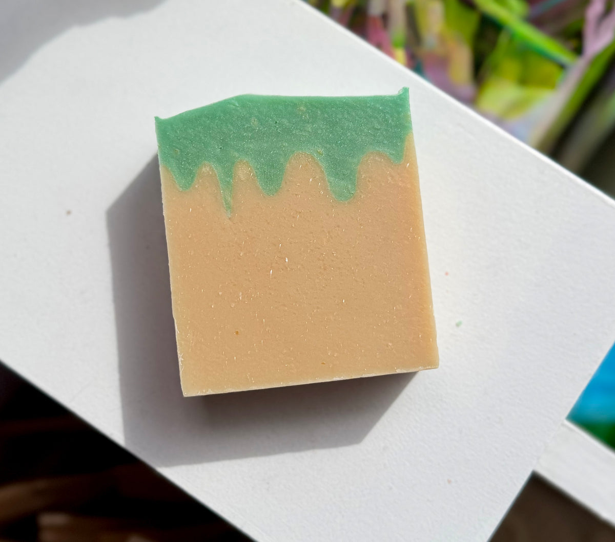 A rectangular bar of soap with a light beige base and a dripping mint green top, resting on a white surface.
