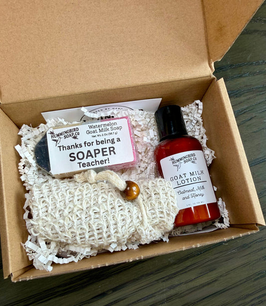 Gift box with pencil shaped soap with label that says "Thanks for being a SOAPER teacher!" next to a beige soap saver bag and a small bottle of lotion.
