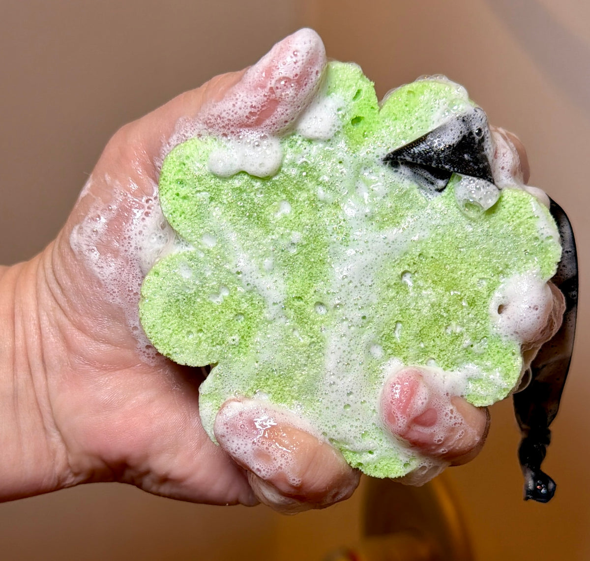 Hand holding green sponge covered in bubbles and lather