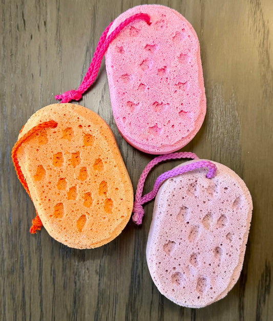 3 sponges in pink, orange, and purple colors with hanging cords on a wooden background.
