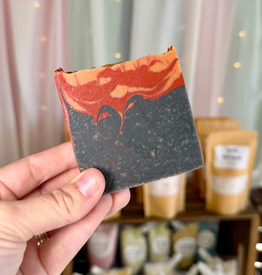 A bar of soap with a black charcoal bottom half resembling smoke, topped with red and orange swirls resembling flames.