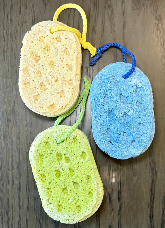 3 sponges in yellow, blue and green colors with hanging cords on a wooden background.