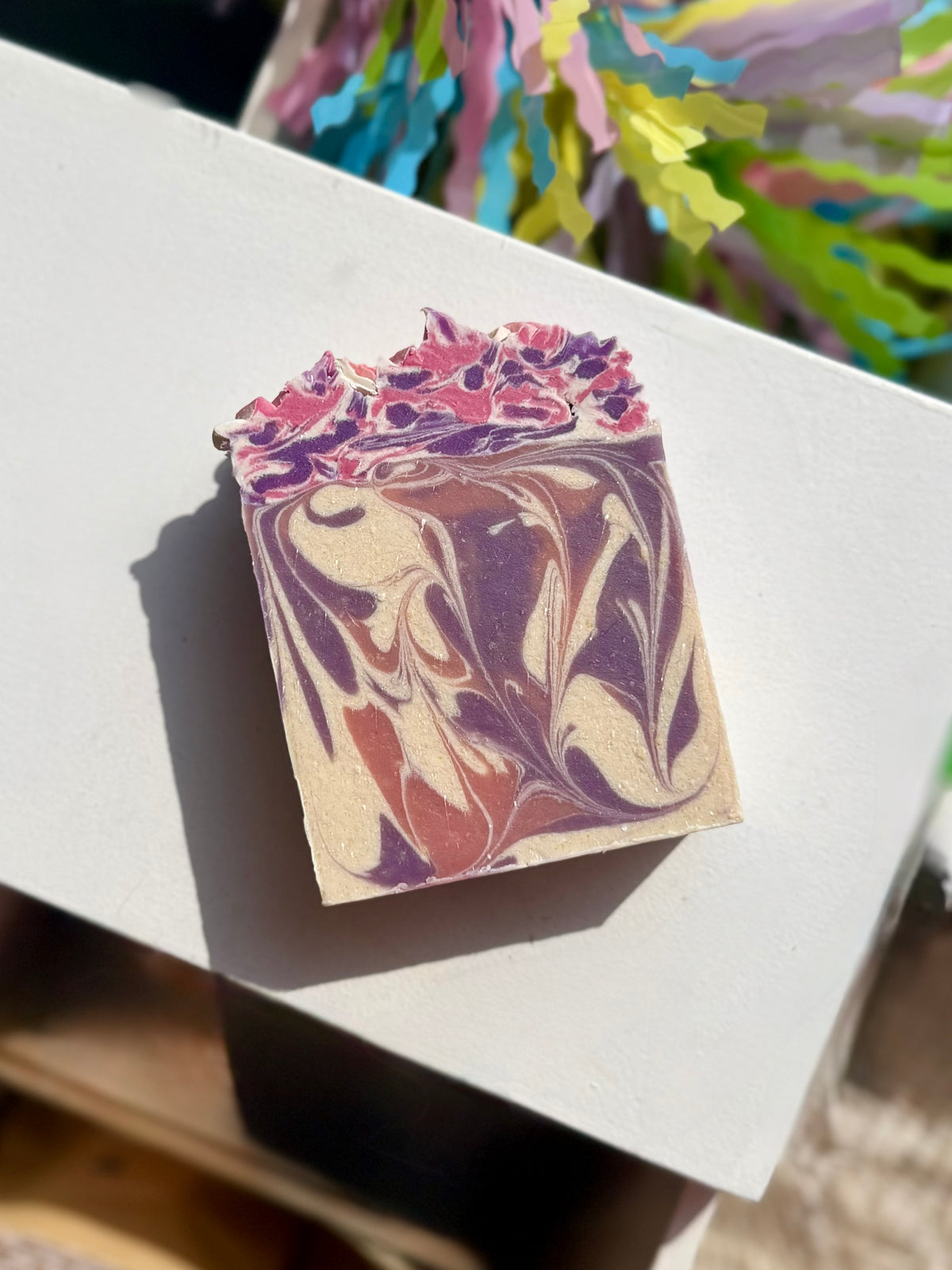 A rectangular soap bar with a marbled swirl pattern of purple, pink, and cream, resting on a white surface. 