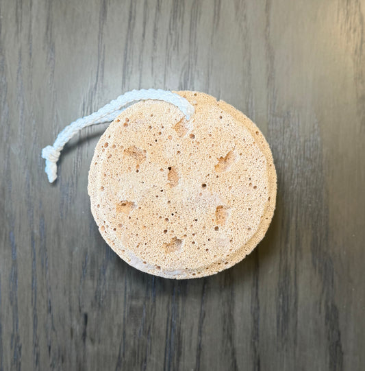 Round natural colored sponge with white hanging cord on a wooden background
