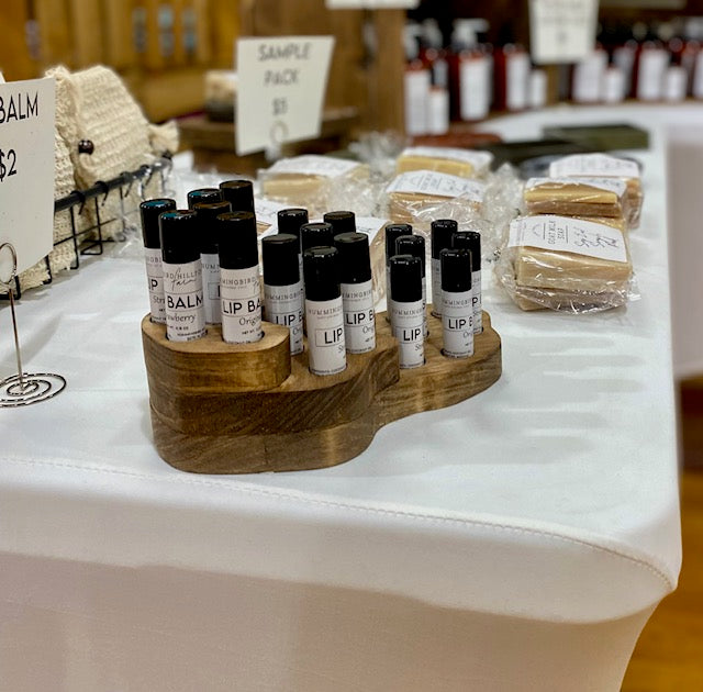 Various labeled black lip balm tubes in a wooden display.