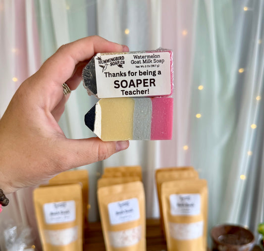Hand holding two pencil shaped soaps. One is wrapped with a label that says "Thanks for being a SOAPER teacher!"